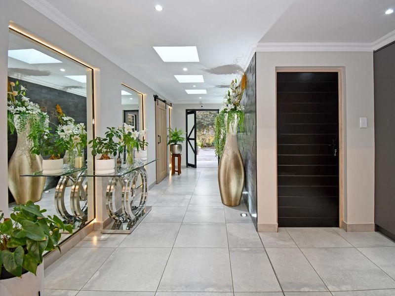 A modern, well-lit hallway featuring large format floor tiles, skylights, a textured feature wall, and sleek built-in cabinetry.