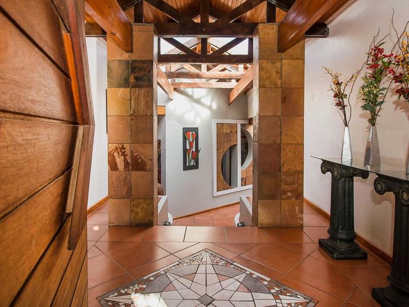 Welcoming entrance hall featuring exposed timber roof trusses, stone-clad pillars, and decorative terracotta flooring with a central mosaic inlay.