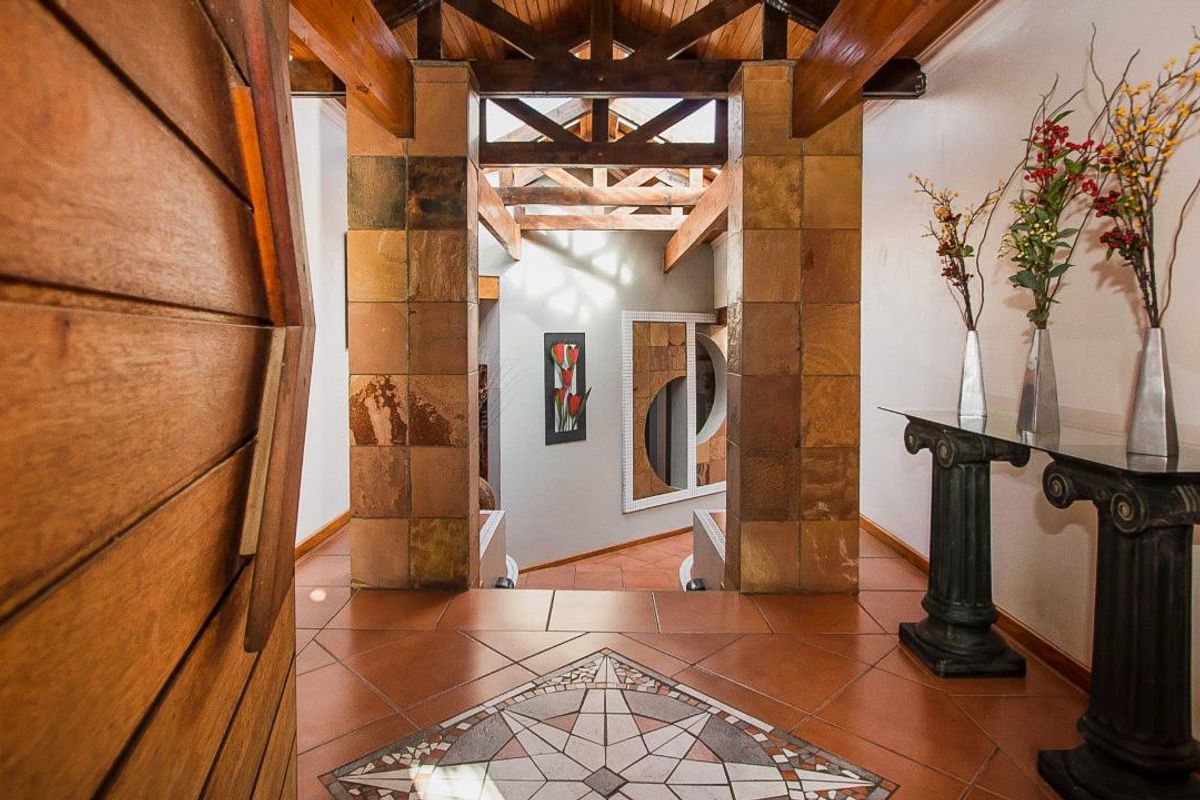 Welcoming entrance hall featuring exposed timber roof trusses, stone-clad pillars, and decorative terracotta flooring with a central mosaic inlay.