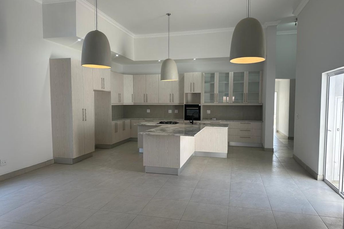 Spacious open-plan kitchen featuring light wood cabinetry, a central island with a built-in hob, stone countertops, and modern pendant lighting.