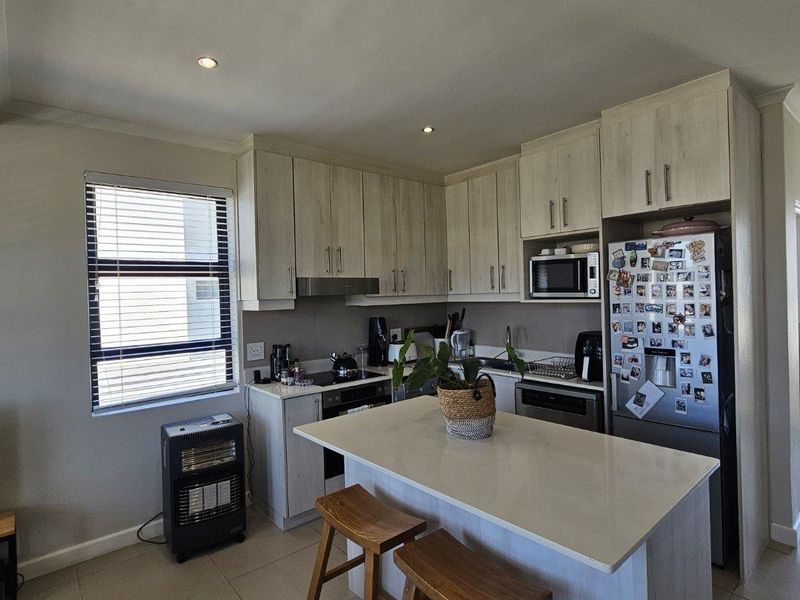 Modern kitchen featuring light wood-finish cabinetry, stone countertops, a central island with breakfast seating, and integrated appliances.