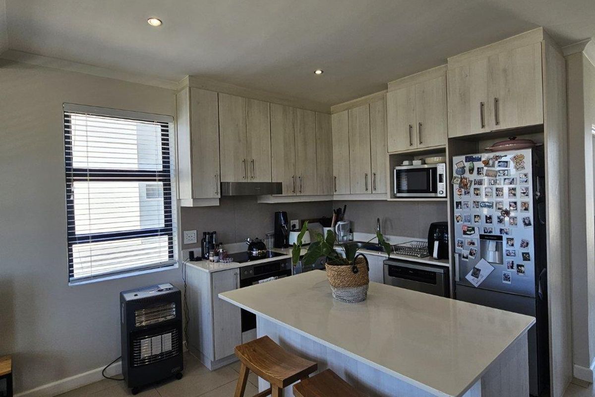 Modern kitchen featuring light wood-finish cabinetry, stone countertops, a central island with breakfast seating, and integrated appliances.