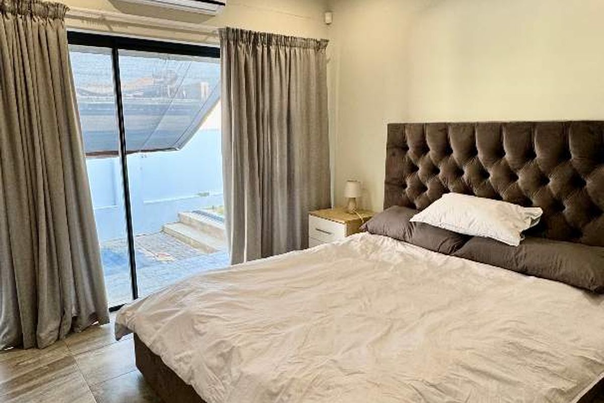 A well-maintained bedroom featuring tiled flooring, a wall-mounted air conditioning unit, and sliding glass doors providing direct access to an outdoor patio area.