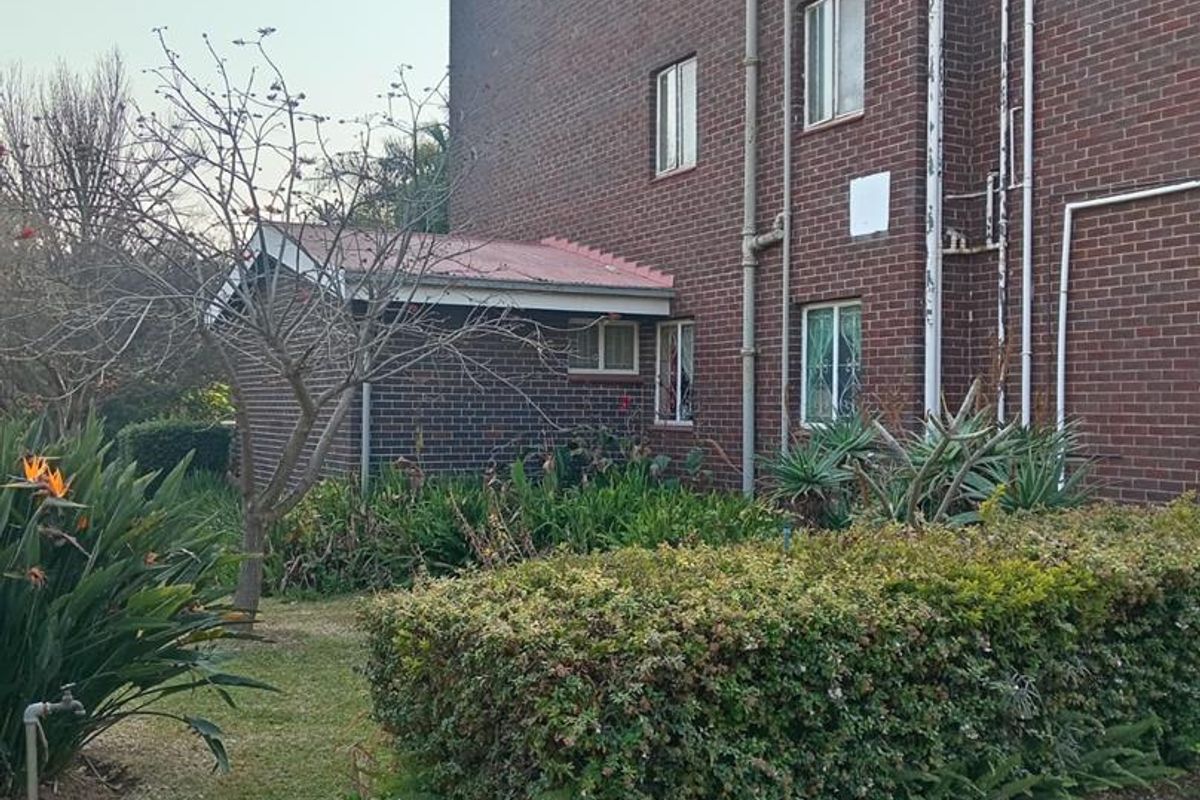 Rear view of the apartment building featuring a brick facade, external plumbing, and a well-maintained garden area with established hedges.