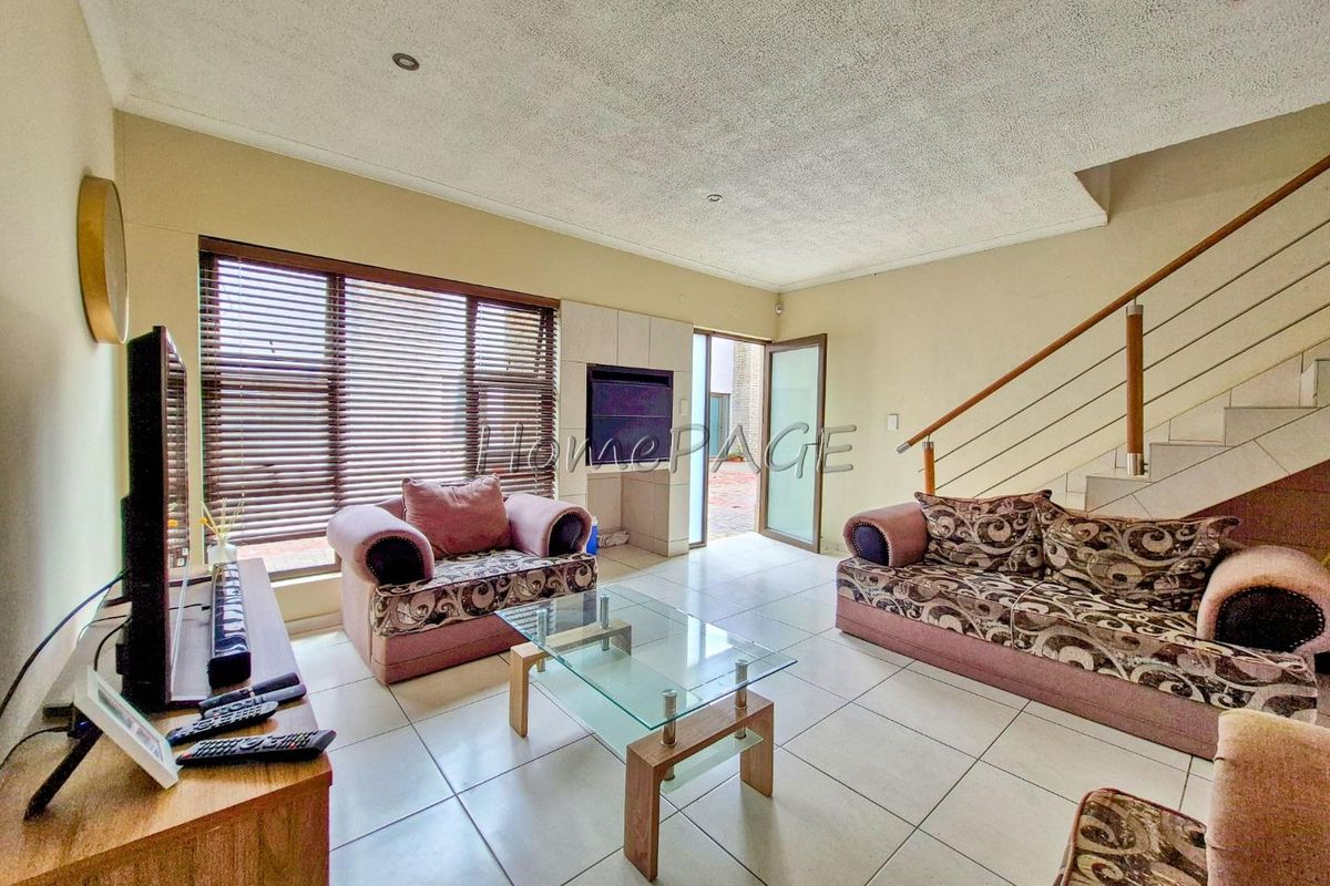 Spacious living room featuring tiled flooring, recessed lighting, and a staircase with a wooden handrail, leading to an outdoor patio area.