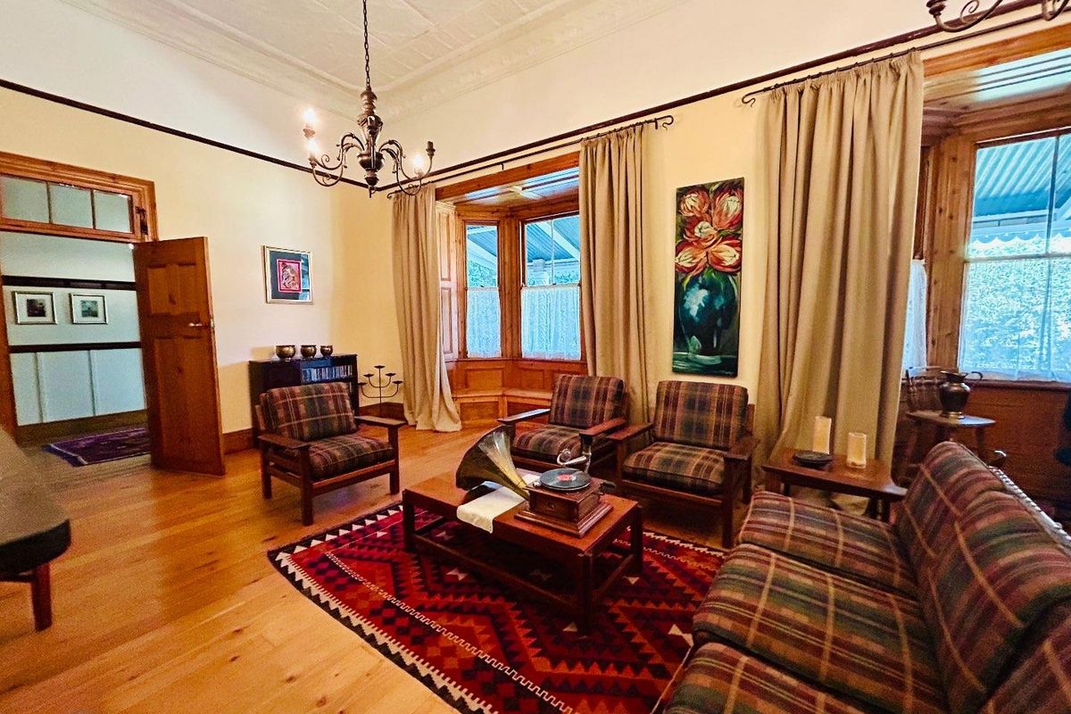 A classic living room featuring polished timber flooring, ornate pressed metal ceilings, and a large bay window with timber framing.