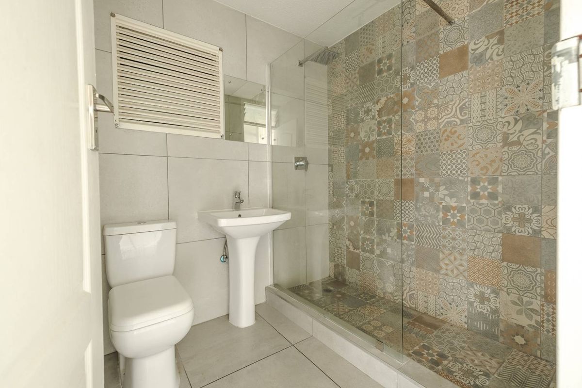 Modern bathroom featuring a glass-enclosed walk-in shower with decorative patterned tiling, a pedestal basin, and a standard toilet.