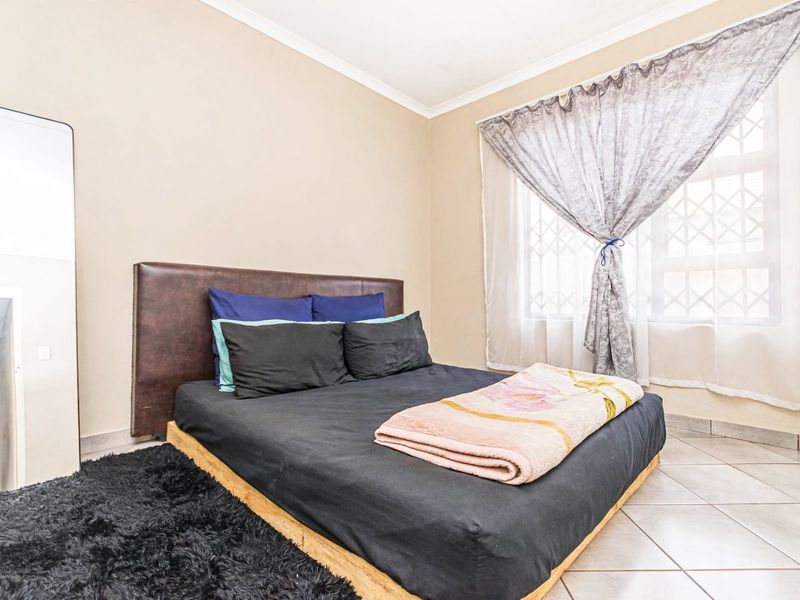 A functional bedroom featuring tiled flooring, a security gate on the window, and neutral wall finishes.