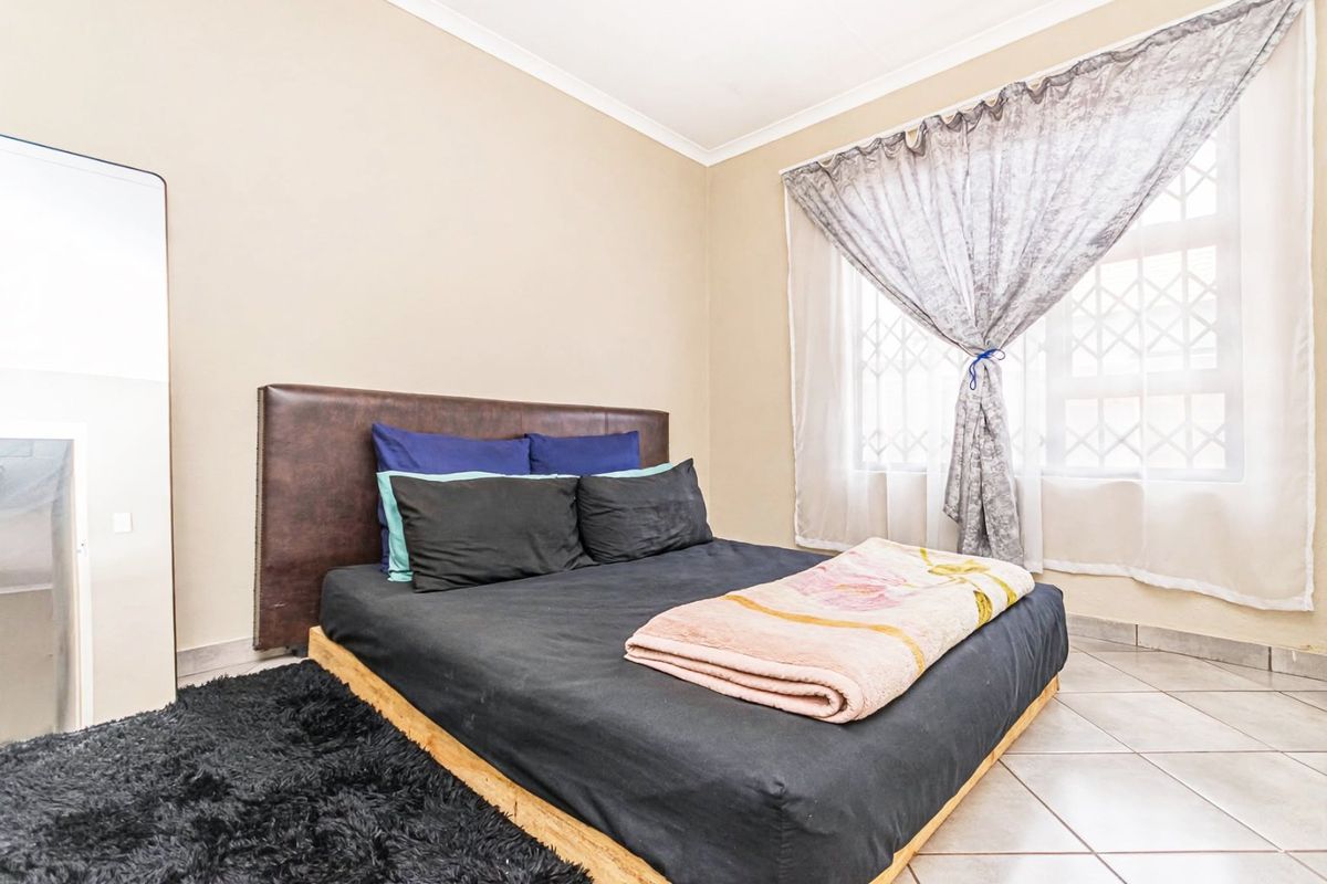 A functional bedroom featuring tiled flooring, a security gate on the window, and neutral wall finishes.