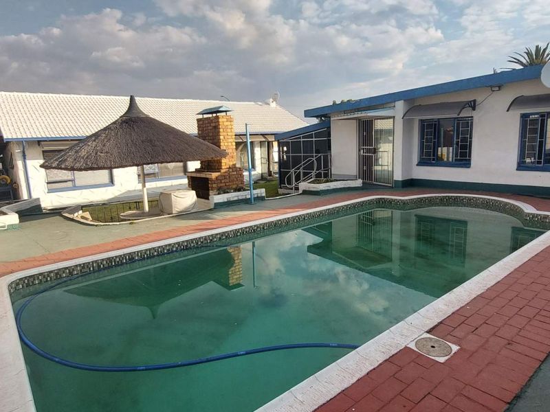 Outdoor pool area featuring a swimming pool, brick built-in braai, and a thatched lapa, set within a paved courtyard.