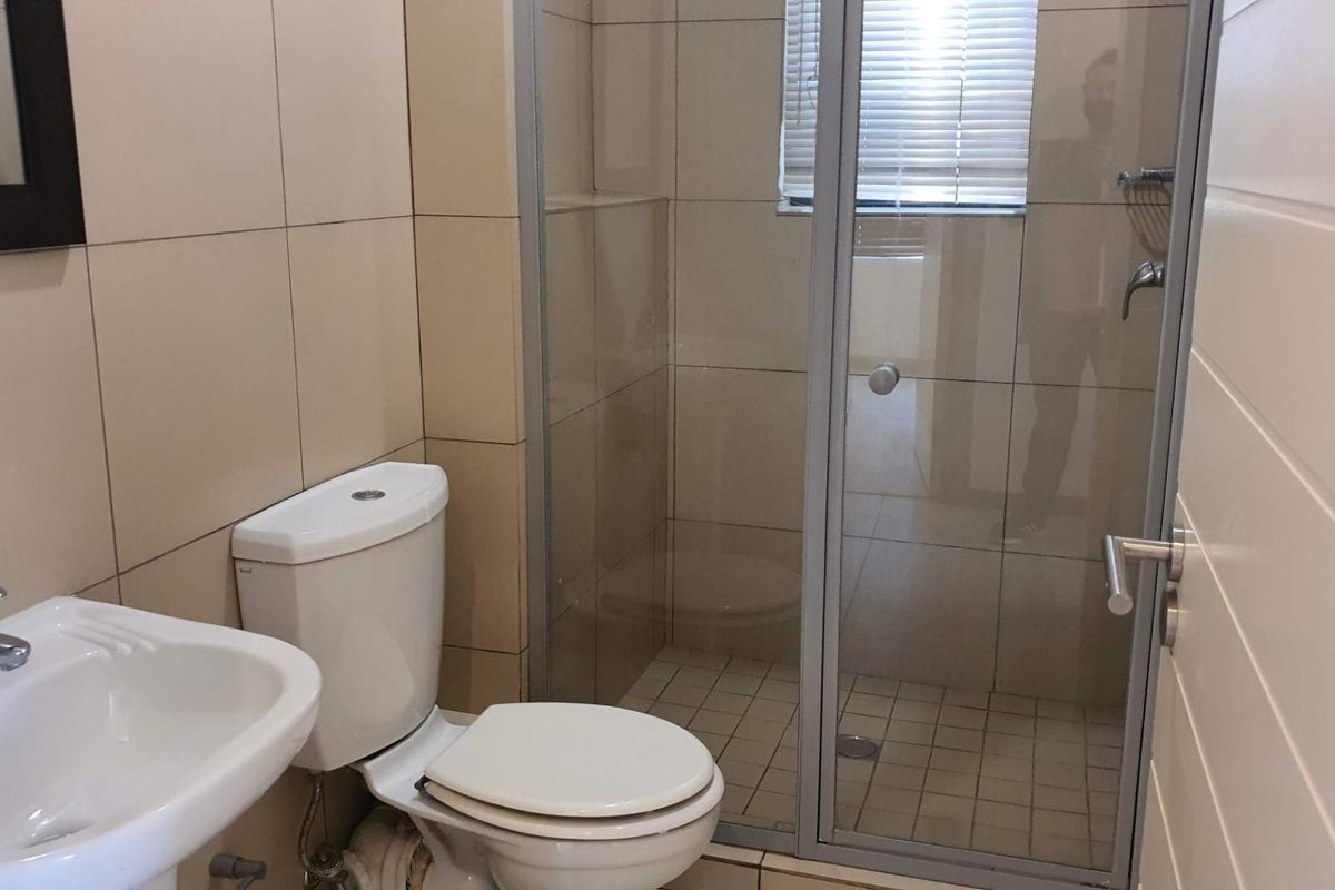 A functional bathroom featuring a glass-enclosed shower, pedestal basin, and toilet with neutral wall tiling.