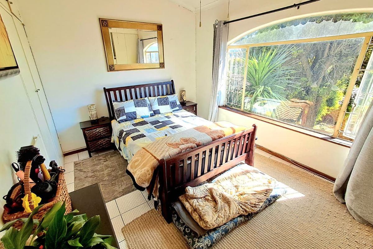 A bedroom featuring tiled flooring, built-in cupboards, and a large arched window providing natural light and garden views.