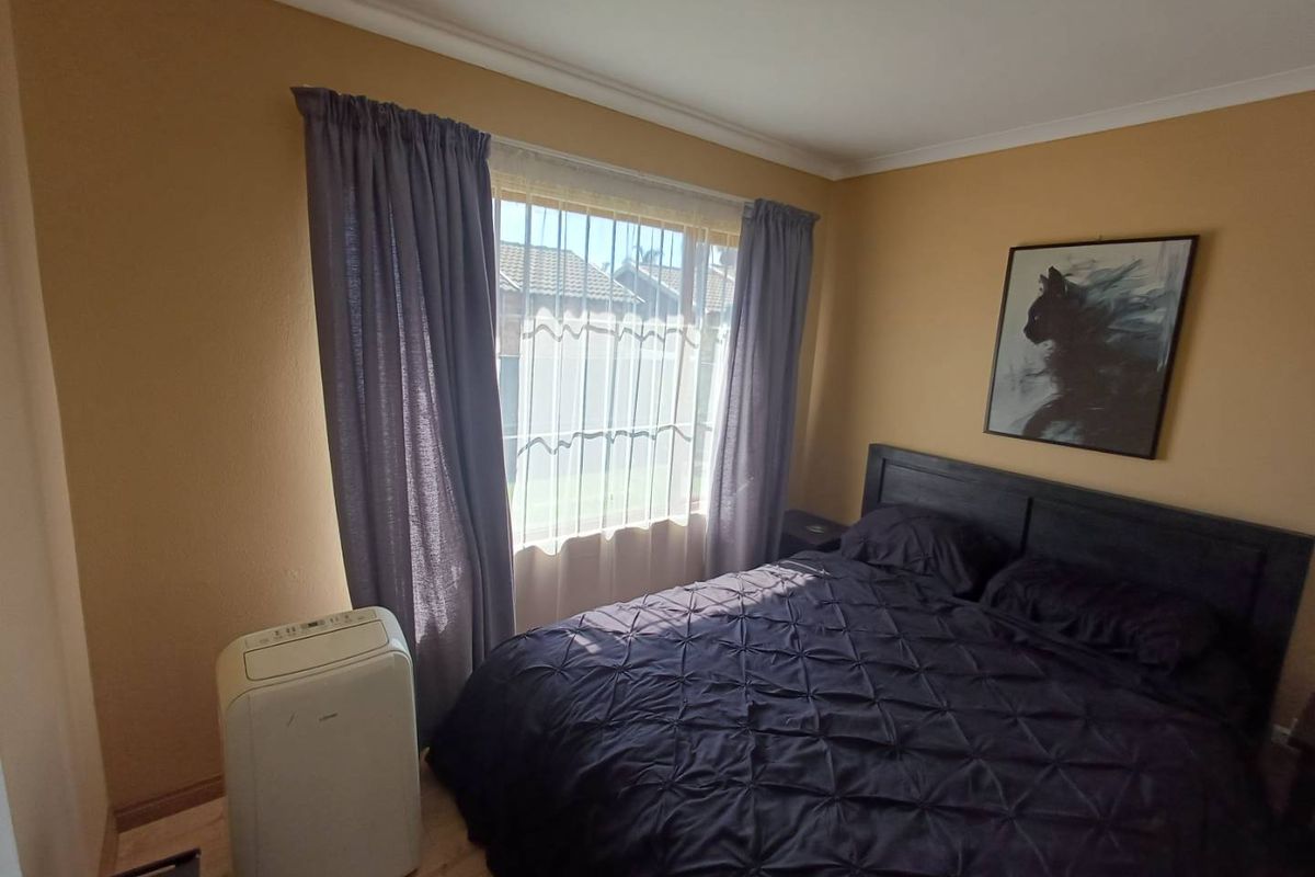 A cozy bedroom featuring neutral wall tones, laminate flooring, and a large window that allows for natural light.