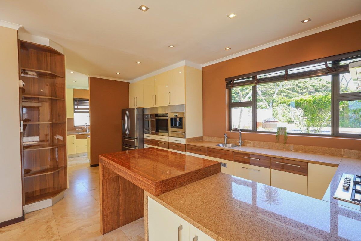 Modern kitchen featuring granite countertops, built-in cabinetry, integrated appliances, and a wooden breakfast bar, with a view into the adjacent scullery area.