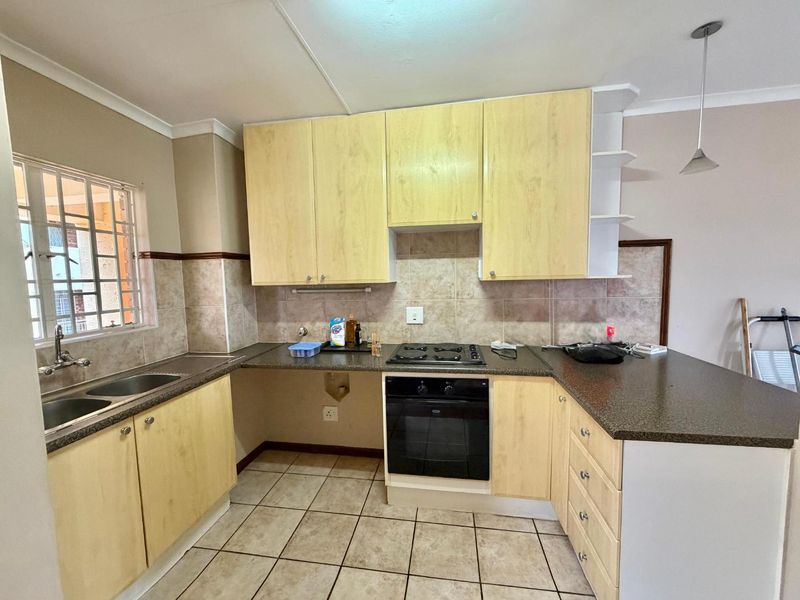 A functional kitchen featuring light wood-finish cabinetry, dark laminate countertops, a built-in oven with gas hob, and tiled flooring throughout.