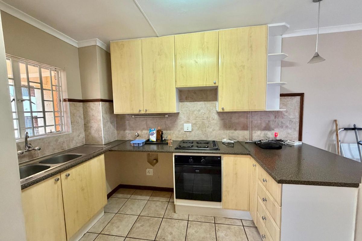 A functional kitchen featuring light wood-finish cabinetry, dark laminate countertops, a built-in oven with gas hob, and tiled flooring throughout.