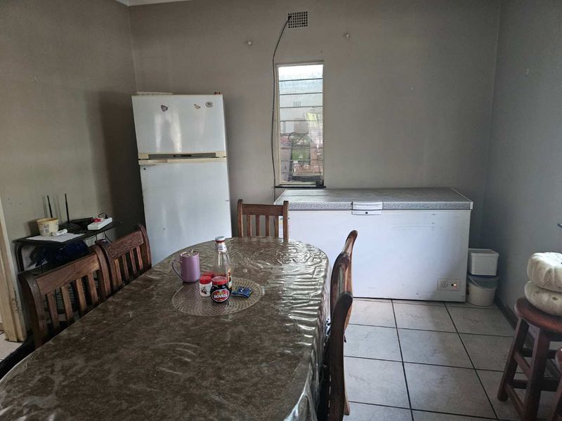 A dining area featuring tiled flooring and a window, currently utilized for storage with visible wall wear and exposed wiring.