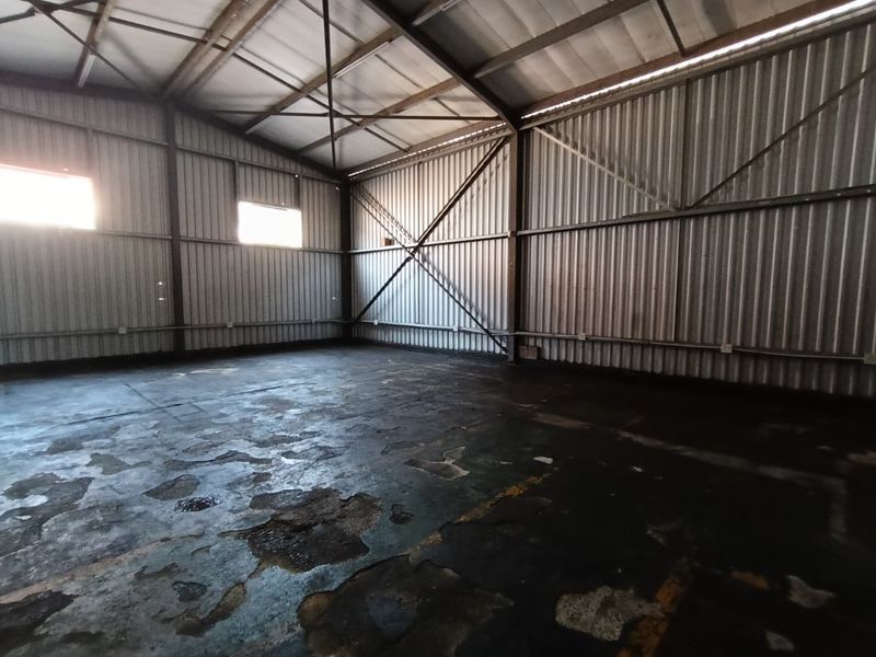 Spacious industrial warehouse unit featuring high ceilings with exposed steel trusses, corrugated metal walls, and a durable concrete floor.