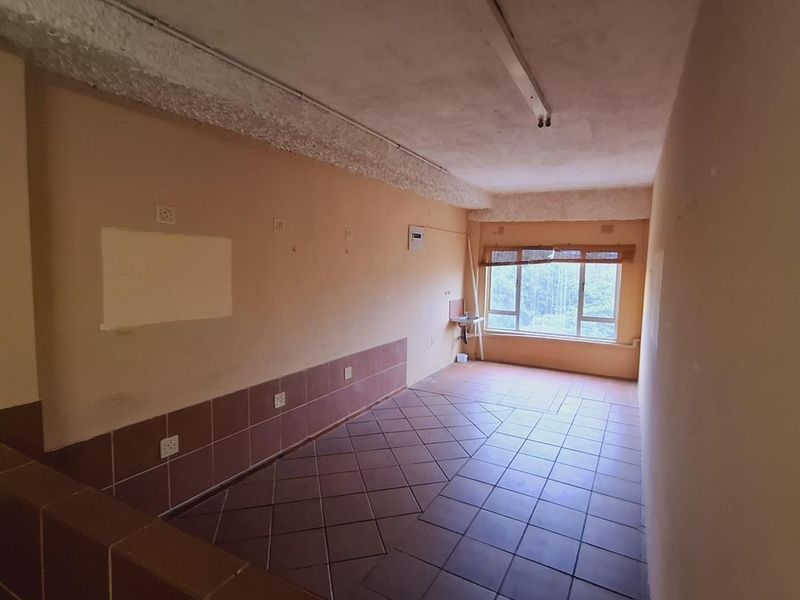 An empty office space featuring tiled flooring, large windows for natural light, and a small wall-mounted basin, requiring cosmetic updates to improve its appeal.