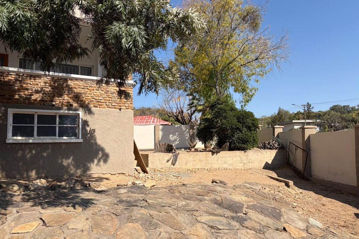 Rear exterior view of the property featuring stone paving, a brick facade, and a retaining wall in a garden setting.