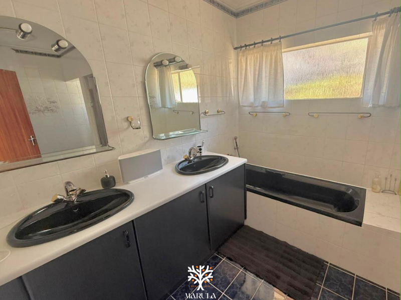 A functional bathroom featuring a double vanity with black basins, a built-in bathtub, and tiled finishes throughout.