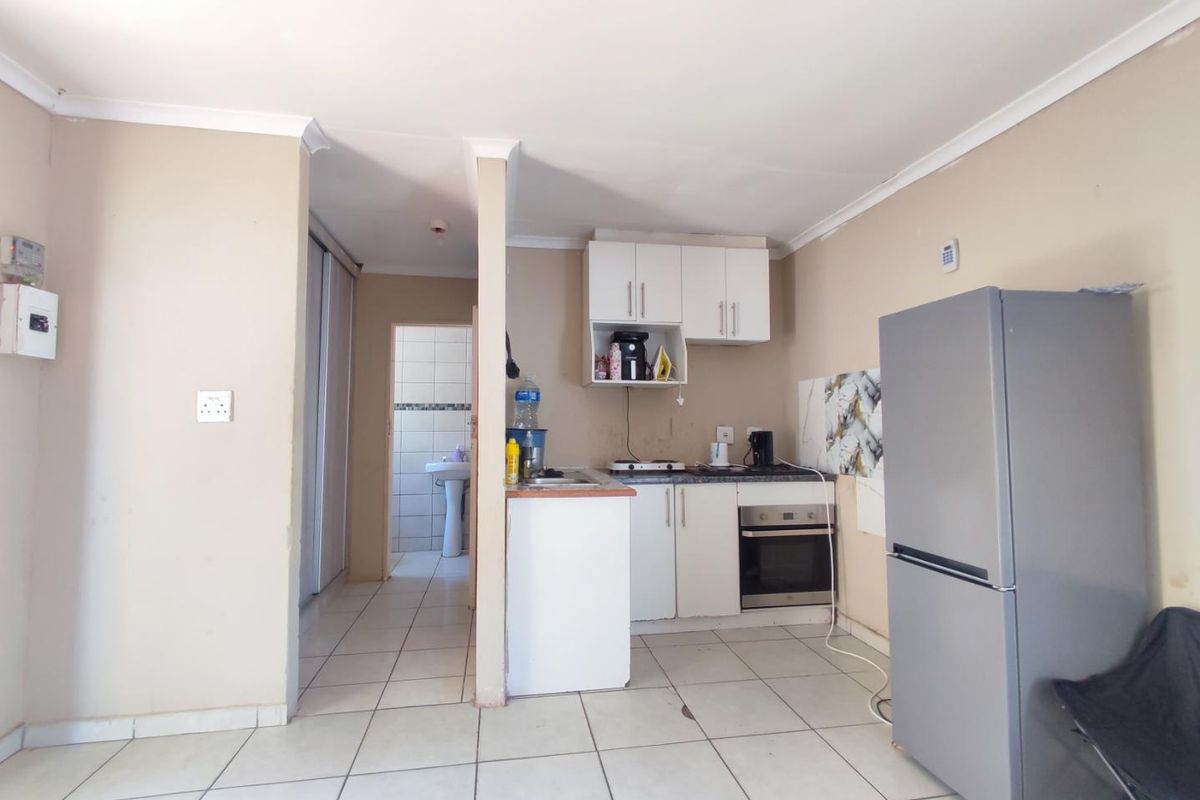 Compact kitchen area featuring built-in cabinetry, integrated oven, and tiled flooring, with an adjacent hallway leading to a bathroom.
