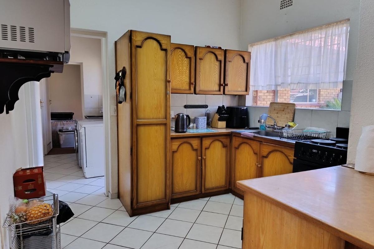 A functional kitchen featuring traditional wooden cabinetry, tiled flooring, and a built-in stove, with an adjacent utility area visible through the doorway.