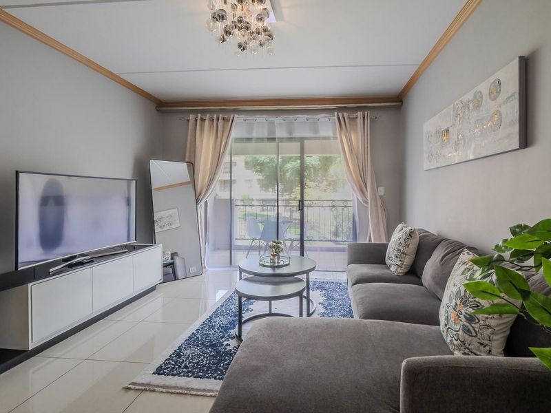 A well-maintained living room featuring polished porcelain floor tiles, crown molding, and a sliding glass door leading to a private balcony.