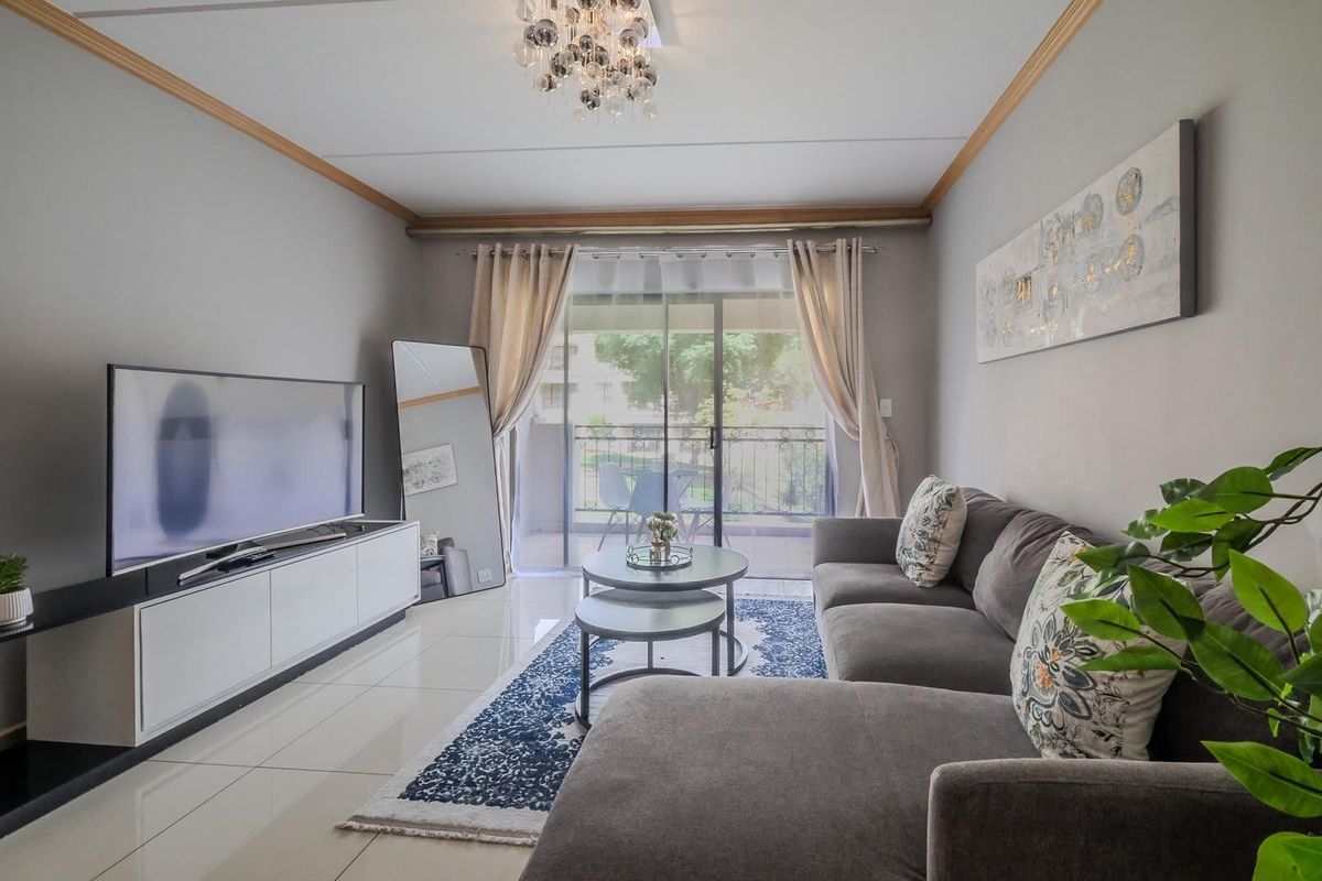 A well-maintained living room featuring polished porcelain floor tiles, crown molding, and a sliding glass door leading to a private balcony.
