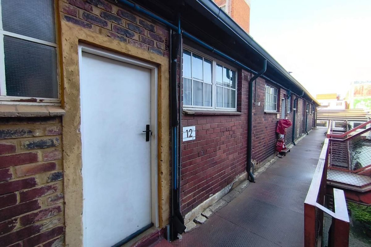 Exterior view of an apartment building showing a brick facade, metal walkway, and access door to unit 12.