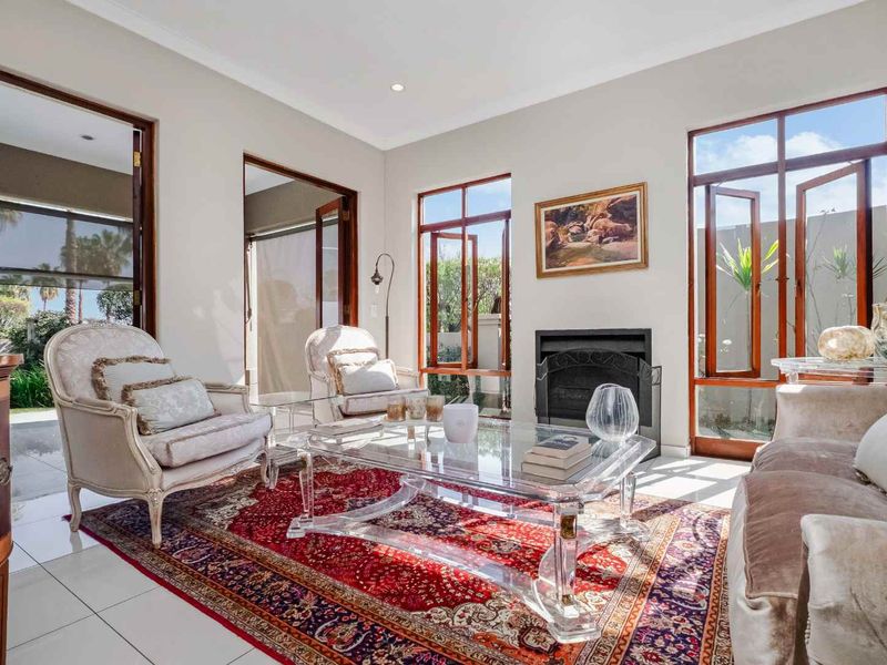 A bright and elegant living room featuring tiled flooring, a built-in fireplace, and large timber-framed windows and doors providing natural light and garden access.
