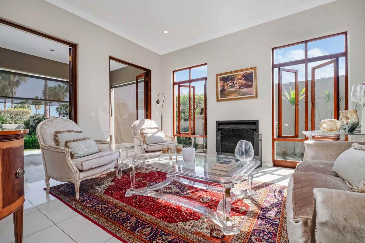 A bright and elegant living room featuring tiled flooring, a built-in fireplace, and large timber-framed windows and doors providing natural light and garden access.