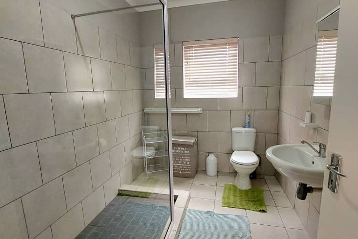 A functional bathroom featuring a glass-enclosed walk-in shower, pedestal basin, and toilet with neutral wall and floor tiling.