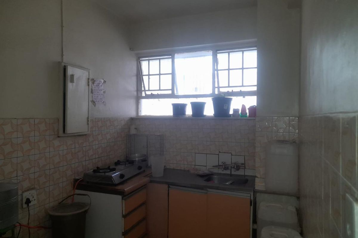 A compact, dated kitchen featuring basic cabinetry, a small sink, and tiled splashbacks, requiring modernization to improve functionality and aesthetic appeal.