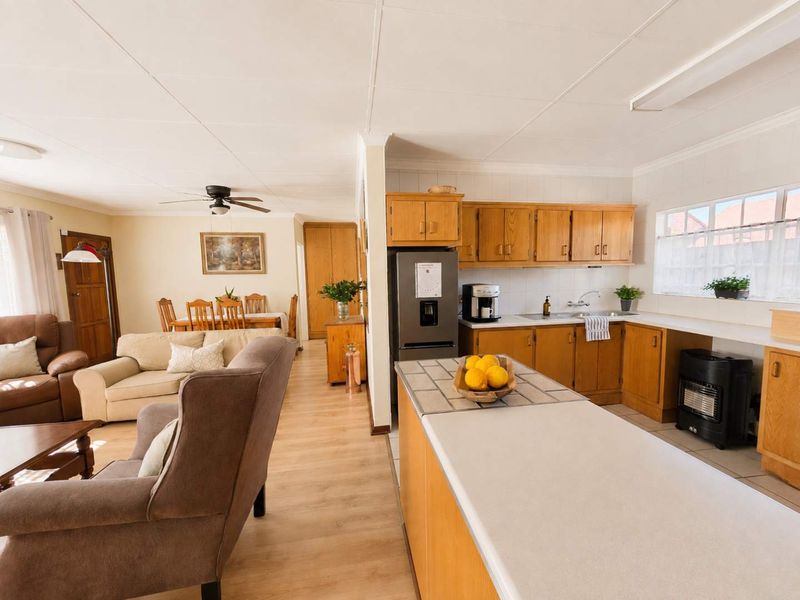 Open-plan living and kitchen area featuring timber cabinetry, laminate flooring, and a functional kitchen layout with a tiled island countertop.