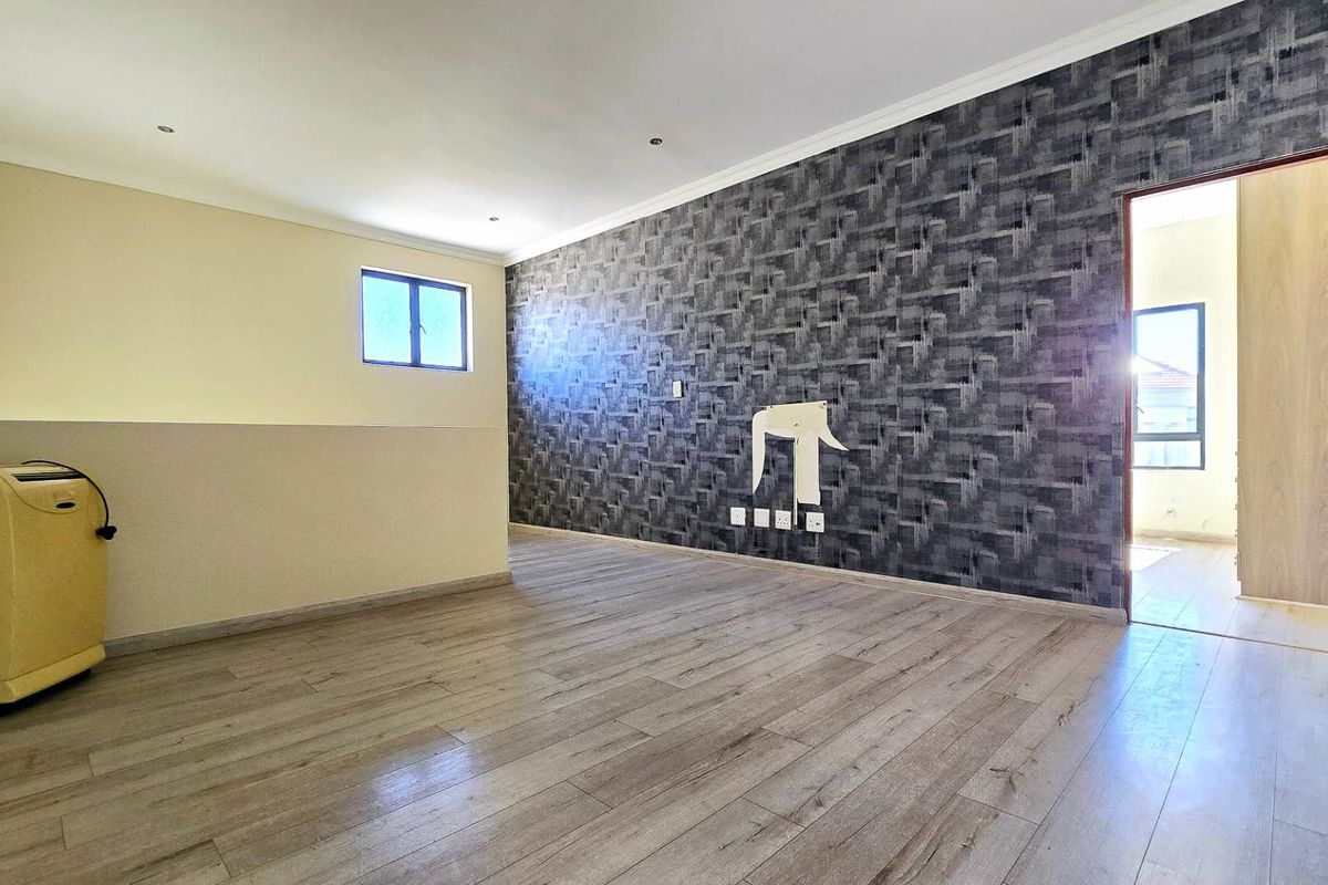 Spacious living area featuring wood-look laminate flooring, a textured feature wall, and recessed ceiling lighting.
