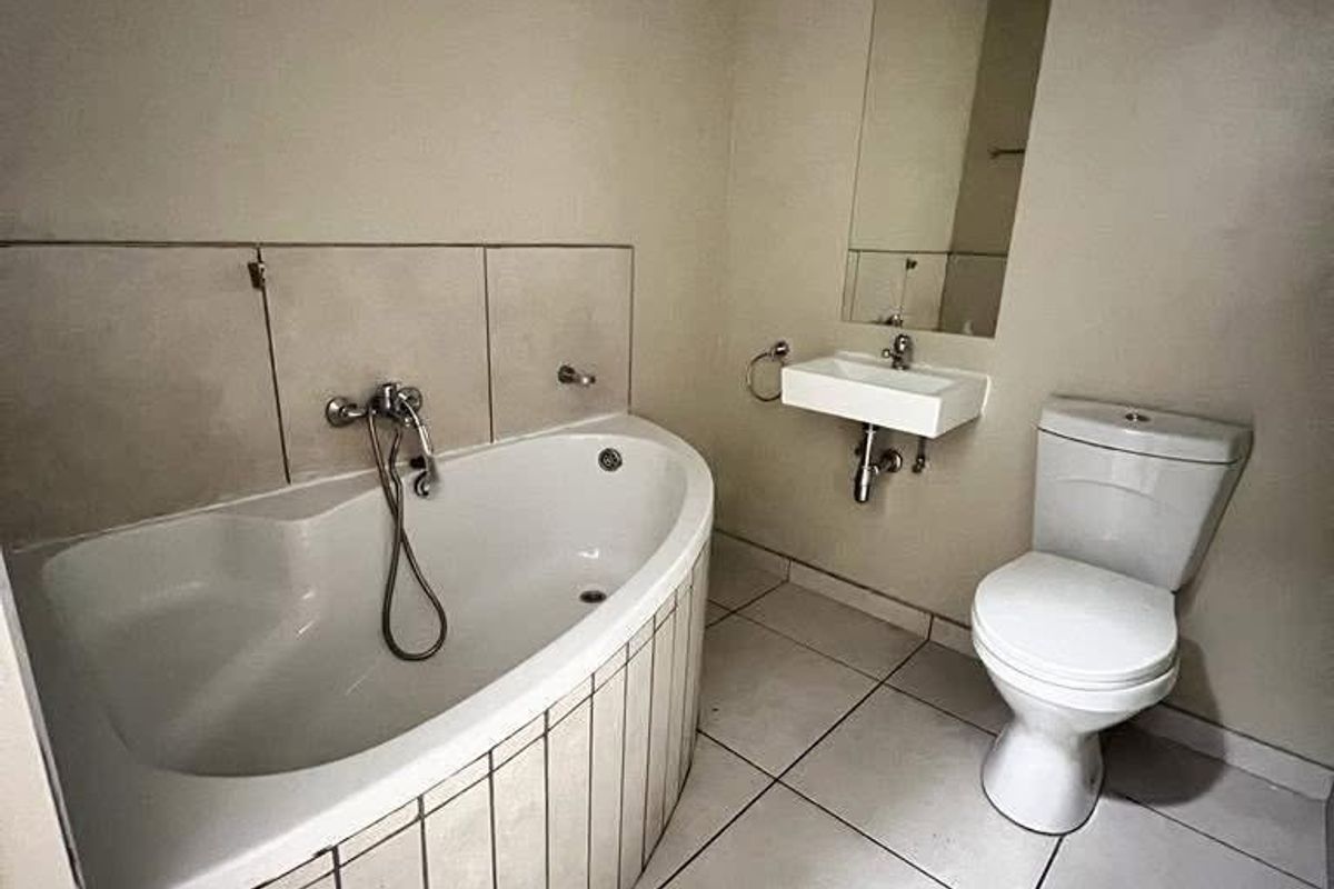 A functional bathroom featuring a corner bathtub, wall-mounted basin, and toilet with neutral tiled finishes.