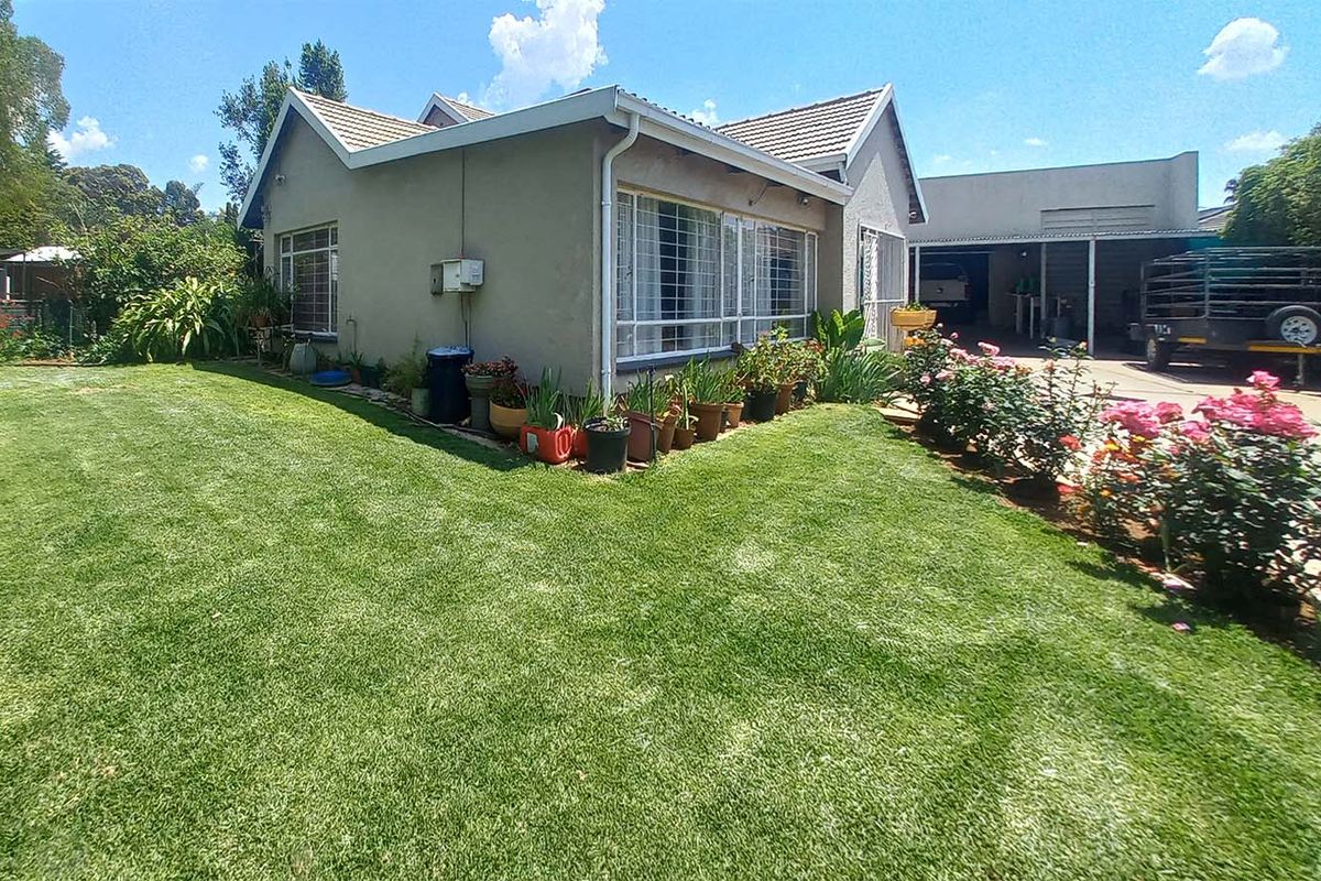 A view of the rear garden and side elevation of the house, featuring a well-maintained lawn, rose bushes, and an attached carport area.