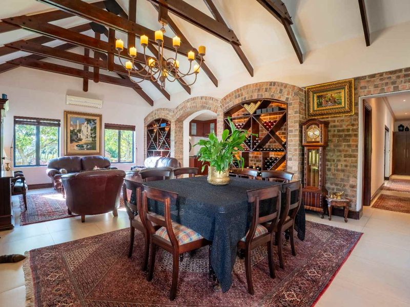 Spacious open-plan living and dining area featuring high vaulted ceilings with exposed timber beams, brick feature walls, and a built-in wine storage display.