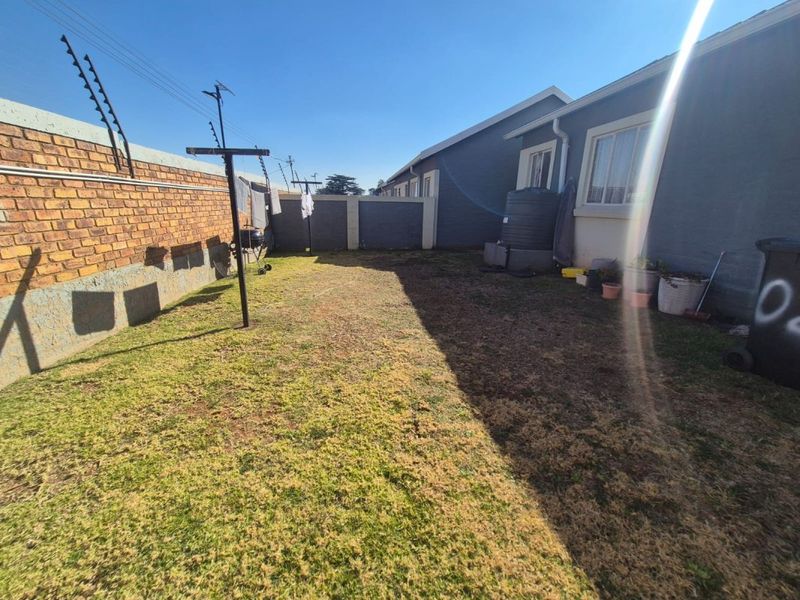 A rear garden area featuring a brick boundary wall with electric fencing, a water storage tank, and a lawn space.