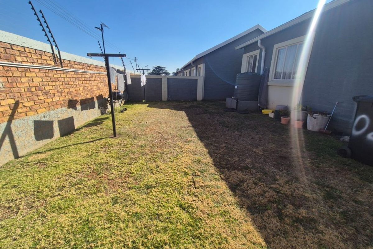 A rear garden area featuring a brick boundary wall with electric fencing, a water storage tank, and a lawn space.