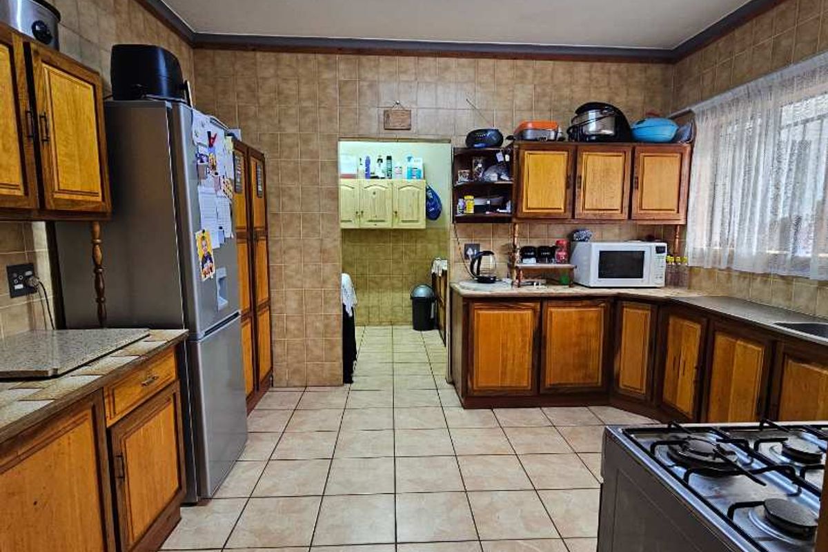 A dated kitchen featuring wooden cabinetry, tiled walls and flooring, and a functional layout with an adjacent scullery area.