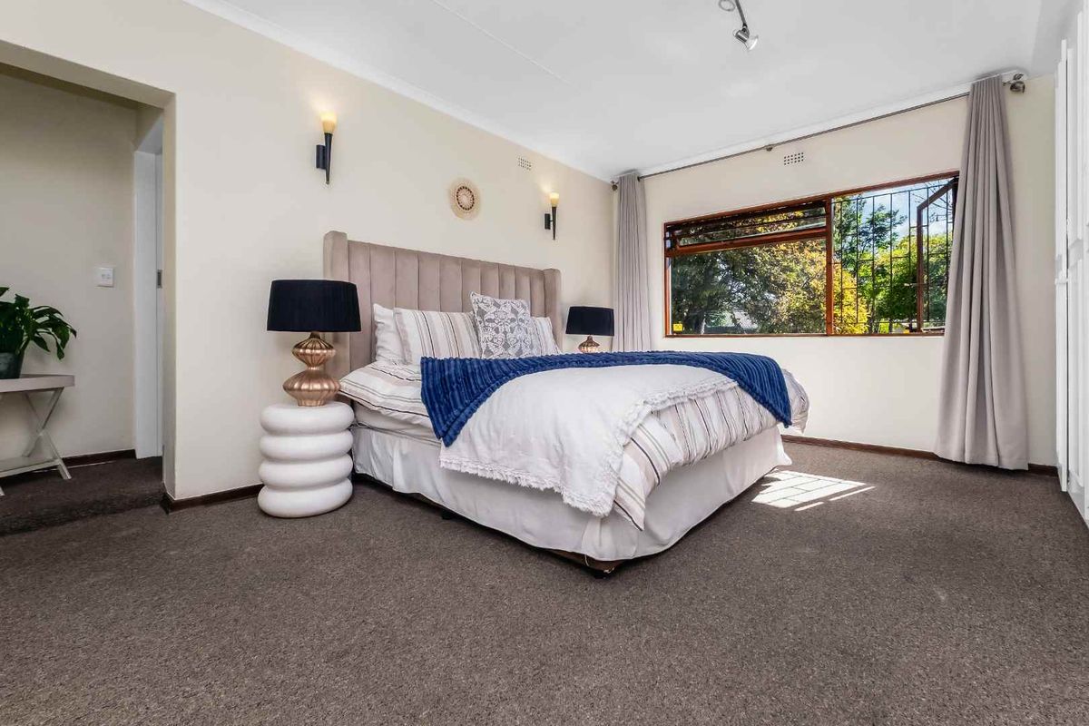 A well-maintained bedroom featuring carpeted flooring, built-in cupboards, and large windows with security bars, providing ample natural light.