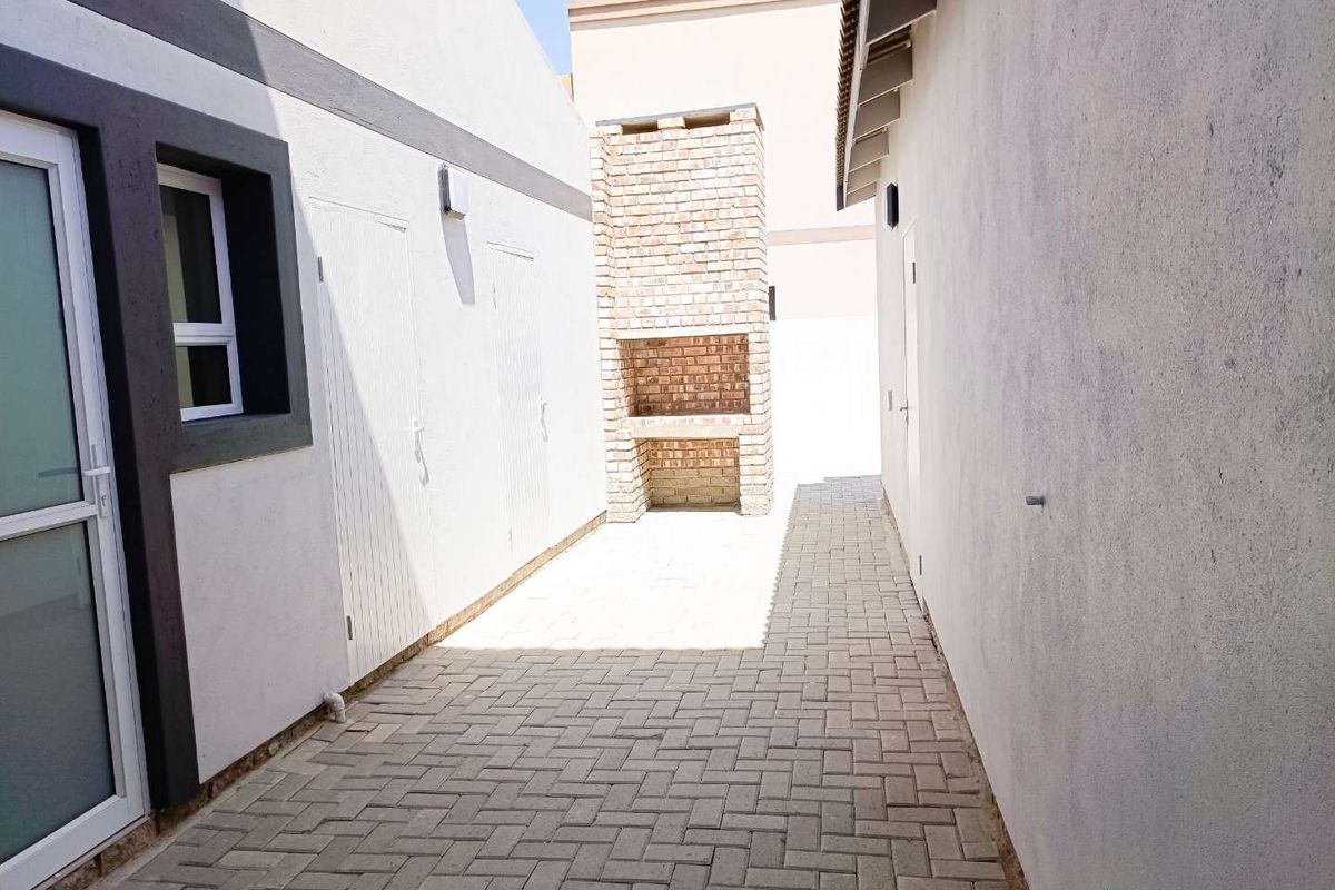 A paved outdoor courtyard area featuring a built-in brick braai or fireplace, situated between two sections of the house.