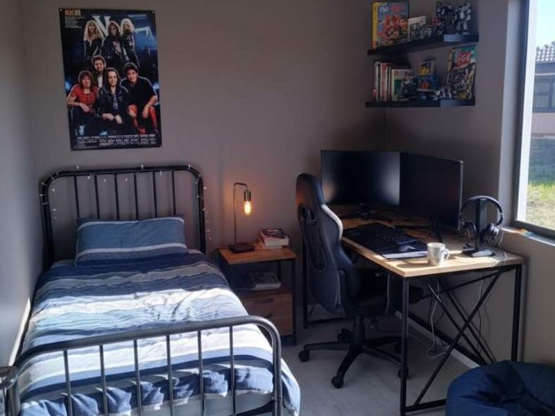 A functional bedroom featuring tiled flooring and wall-mounted shelving, currently utilized as a combined sleeping and workspace area.