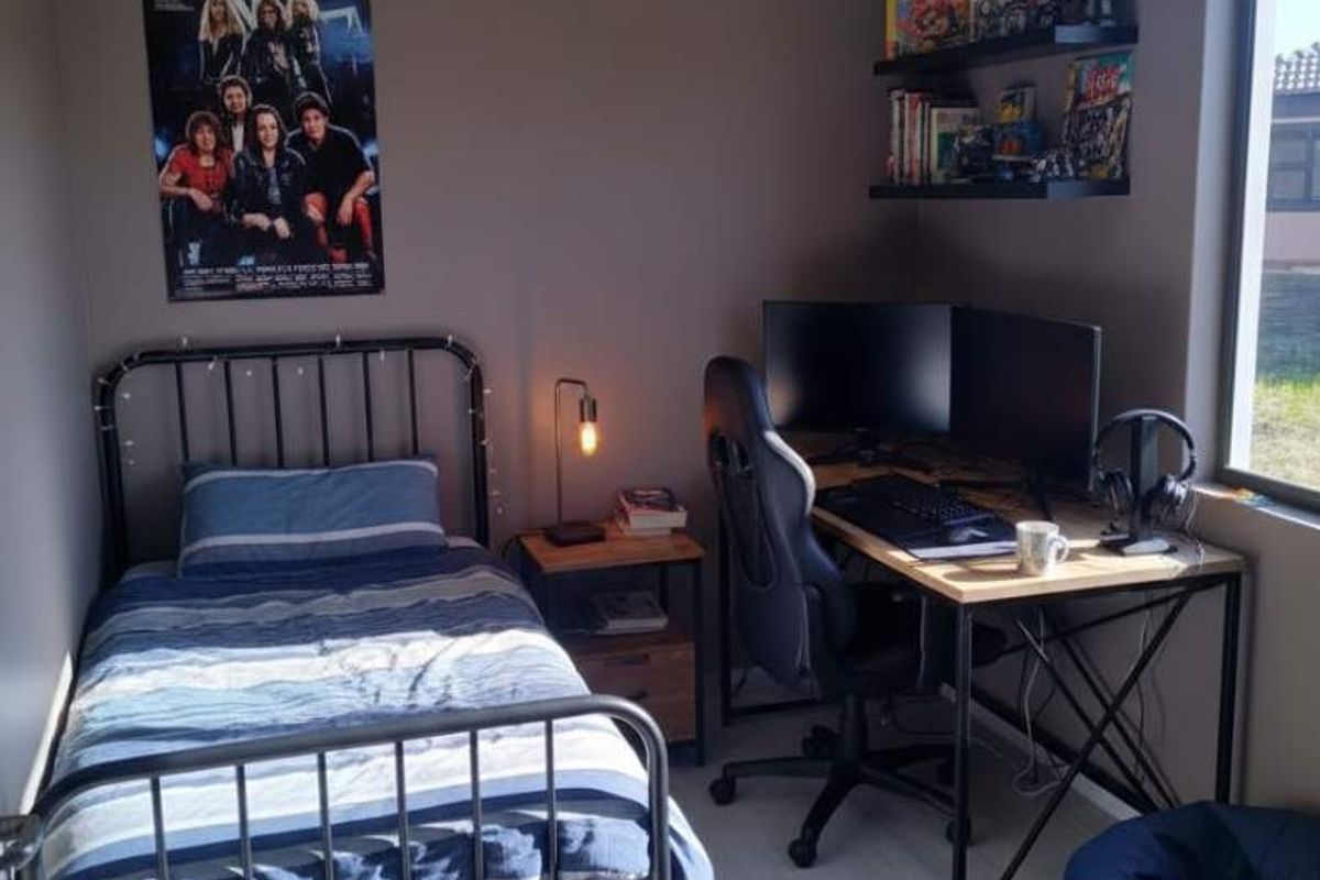 A functional bedroom featuring tiled flooring and wall-mounted shelving, currently utilized as a combined sleeping and workspace area.