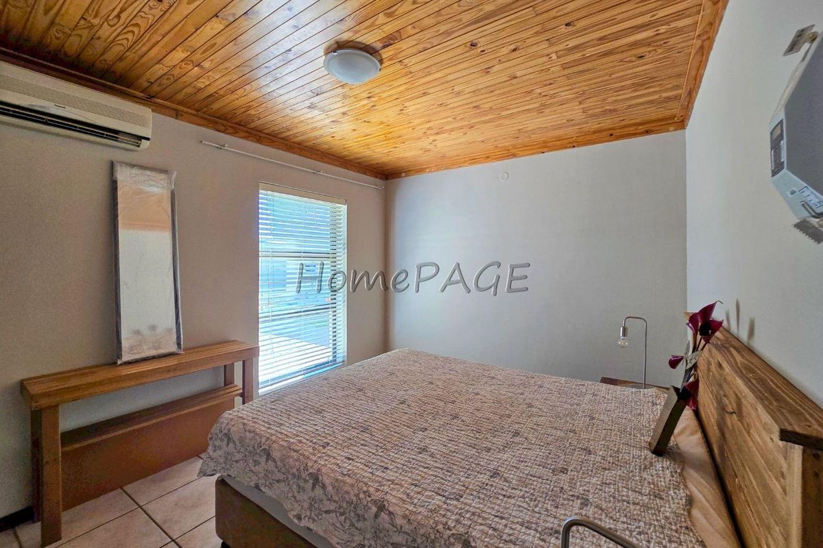 A bedroom featuring a warm timber tongue and groove ceiling, tiled flooring, and a wall-mounted split-system air conditioner.