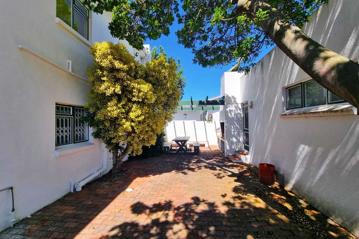 A private rear courtyard featuring brick paving, a built-in braai area, and established trees, providing a secluded outdoor space for relaxation.