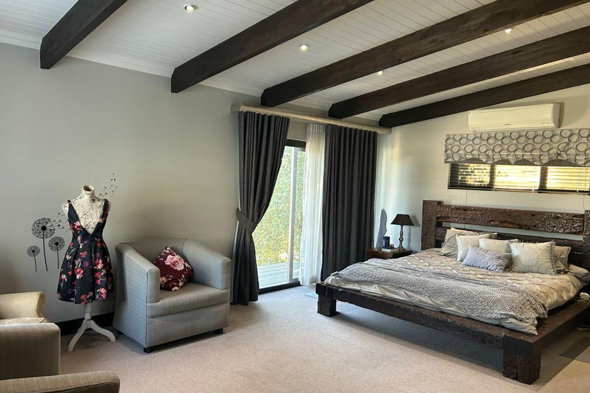 Spacious bedroom featuring exposed timber ceiling beams, recessed lighting, wall-mounted air conditioning unit, and sliding glass doors leading to an outdoor area.