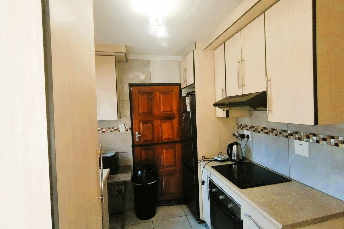 A compact kitchen featuring built-in cabinetry, an electric hob, an extractor fan, and tiled finishes, providing a functional workspace.
